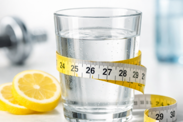 Drinking water help to lose weight concept with a glass of water wrapped in measuring tape and lemon slices on white background
