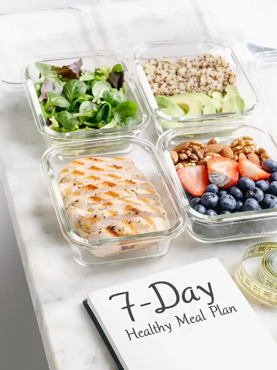 Neatly arranged weekly healthy meal prep on a white table with glass containers, notebook, measuring tape, and water bottle